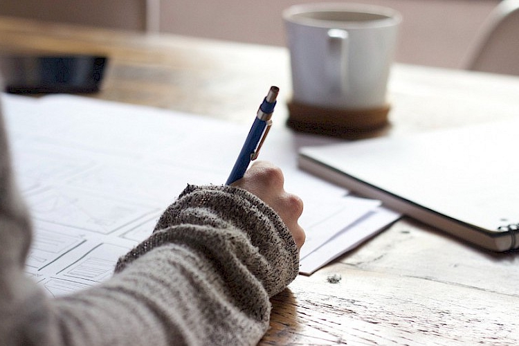 Someone writing, a coffee cup is seen in the distance.